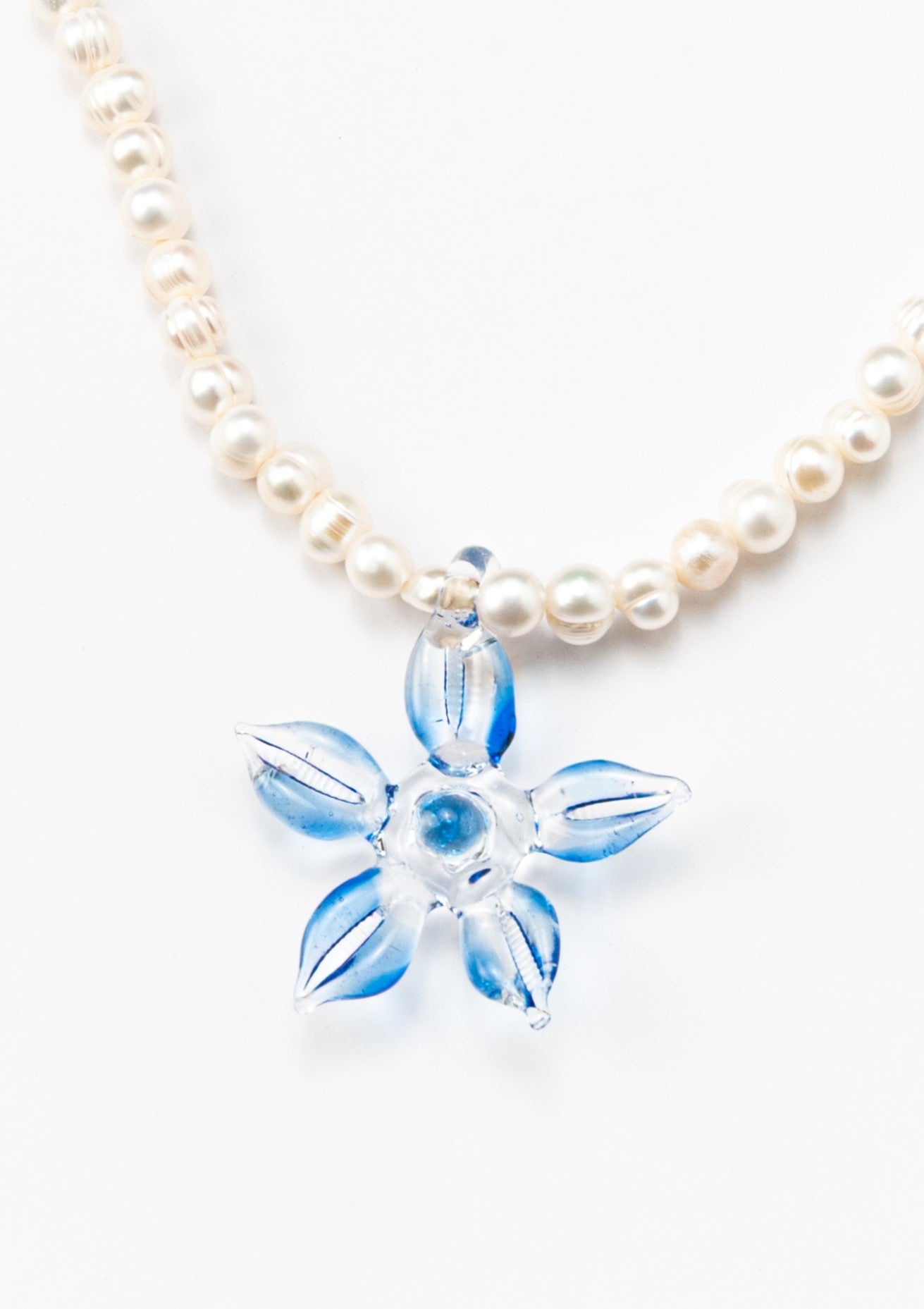 Necklace made of small white river pearls, featuring a gold toggle clasp and a large light blue flower pendant made from recycled glass