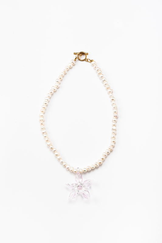 Necklace made of small white river pearls, featuring a gold toggle clasp and a large light pink flower pendant made from recycled glass