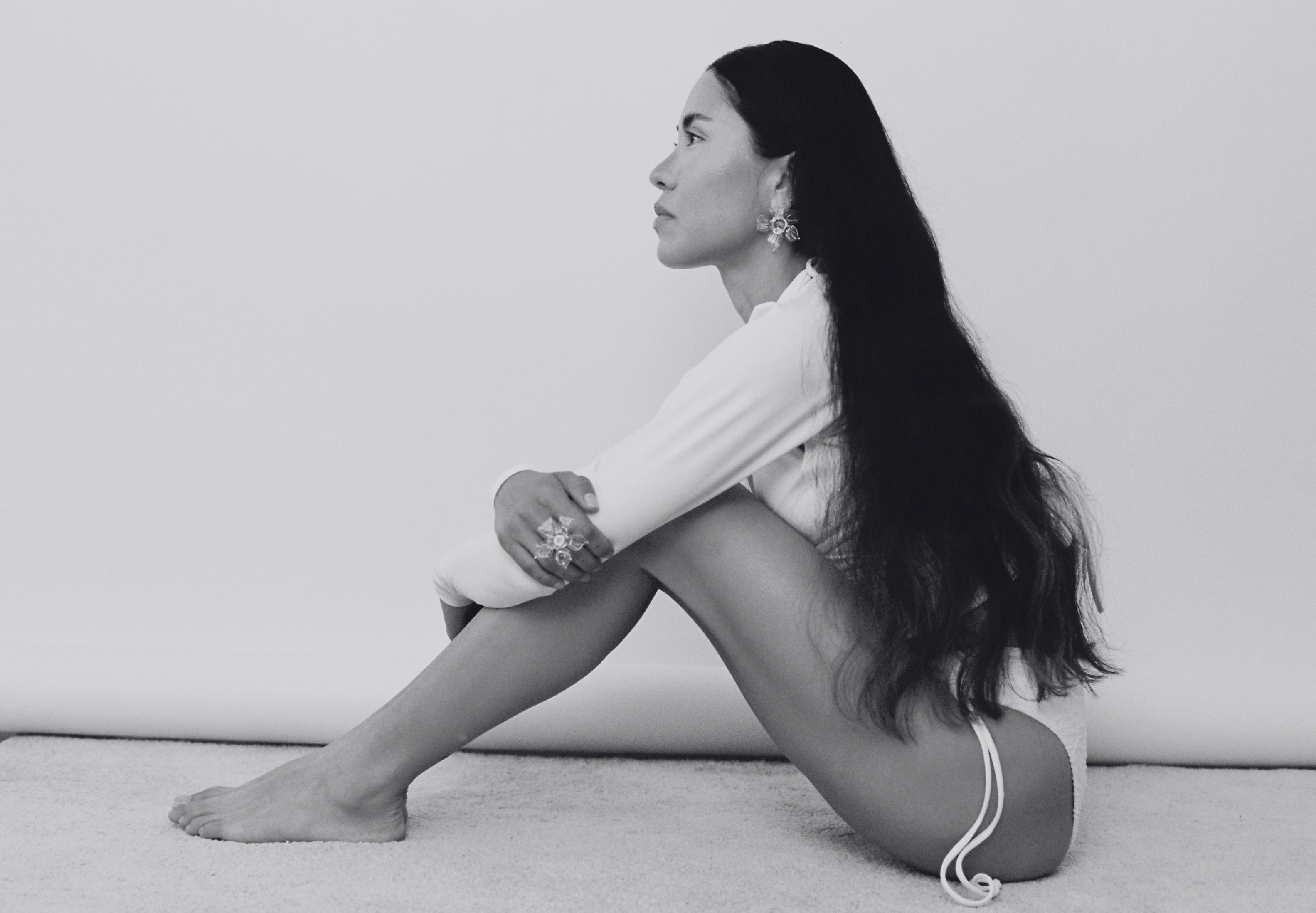 Black and white photo of a person sitting on a couch wearing a white outfit.